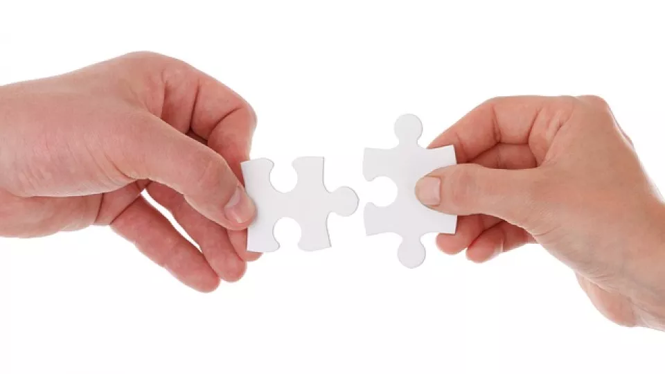 Two hands hold two pieces of a puzzle together. Photo
