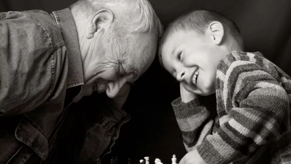 Elderly man and a small boy sit with their heads close to each other and laugh