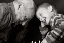 Elderly man and a small boy sit with their heads close to each other and laugh