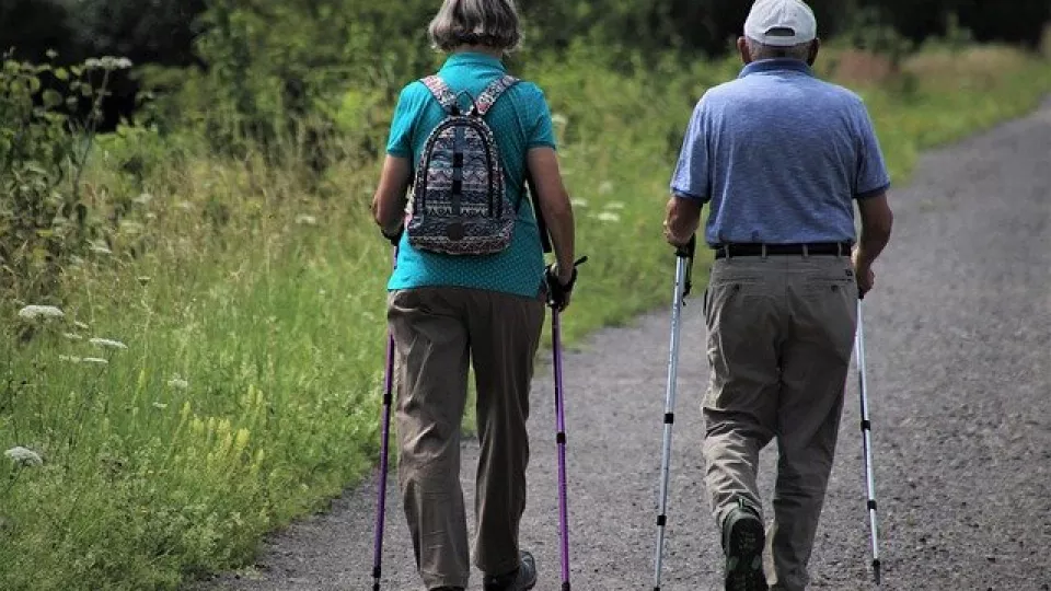 Foto. Två äldre människor går stavgång.