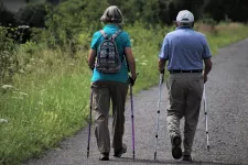 Foto. Två äldre människor går stavgång.